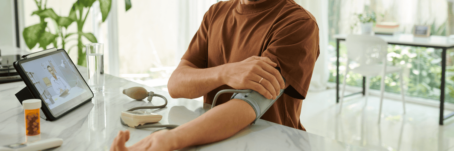 Atacand Price - Atacand Candesartan - Man in brown shirt using a blood pressure monitor while consulting a doctor via tablet.