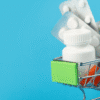 Are International Pharmacies Safe - Online Pharmacy Shopping - Miniature silver shopping cart filled with white medication bottles, blister packs, and syringes on a blue background.