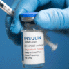 How to Order Diabetes Medications Online Safely - Insulin 100 Units/ml - Gloved hand holding a clear glass medication vial with a blue cap against a blue background.