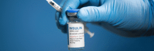 How to Order Diabetes Medications Online Safely - Insulin 100 Units/ml - Gloved hand holding a clear glass medication vial with a blue cap against a blue background.
